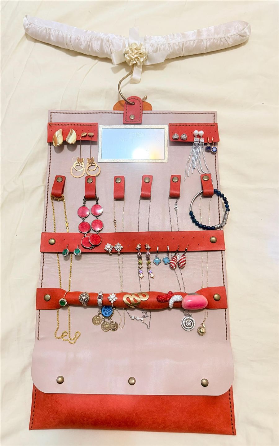An Italian Pueblo leather jewellery organiser roll opened flat to show its stitched compartments and small mirror, with rings and chains laid inside