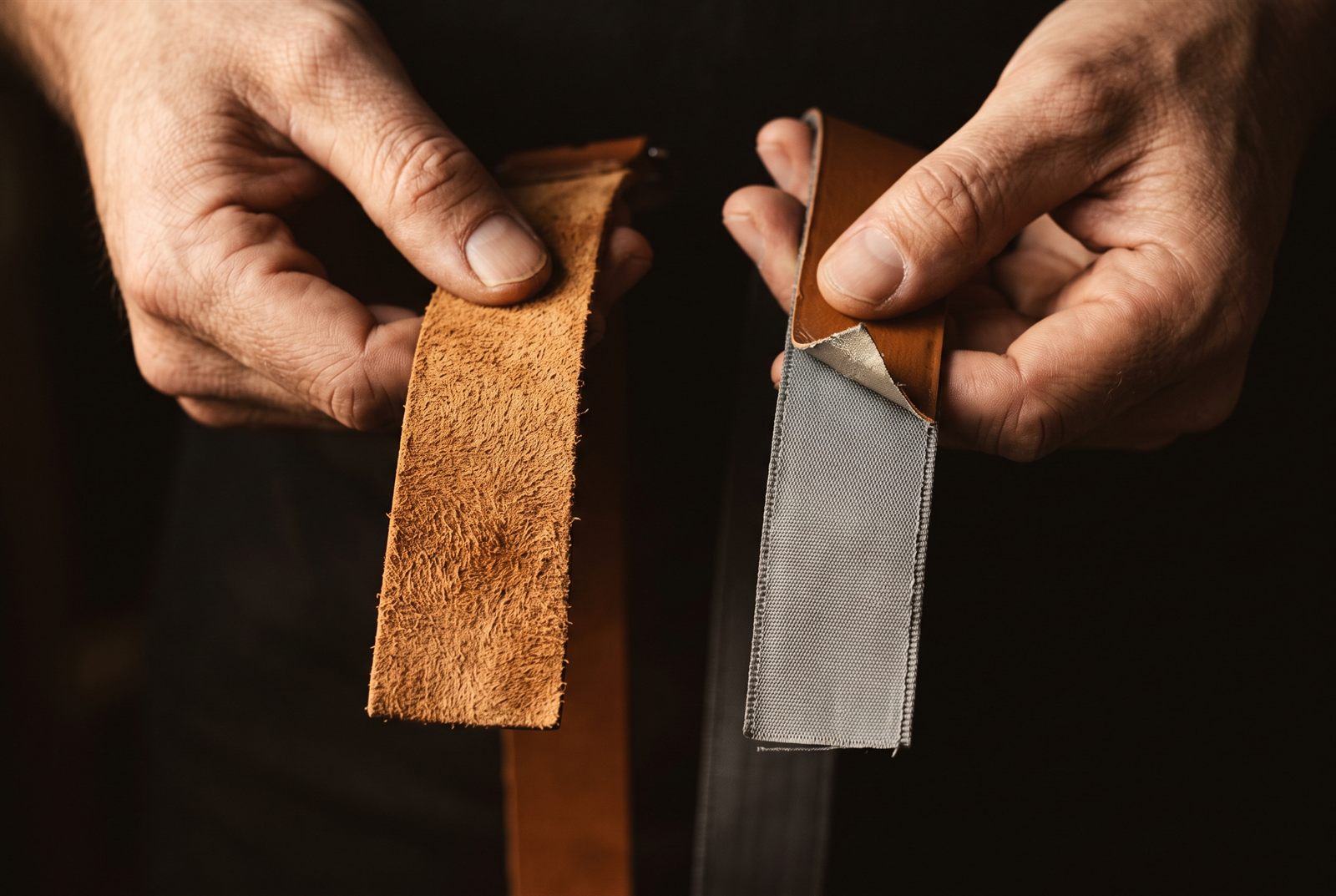 Two leather straps flipped to show their undersides — one with fibrous suede flesh, the other with a grey woven fabric backing peeling from the coating