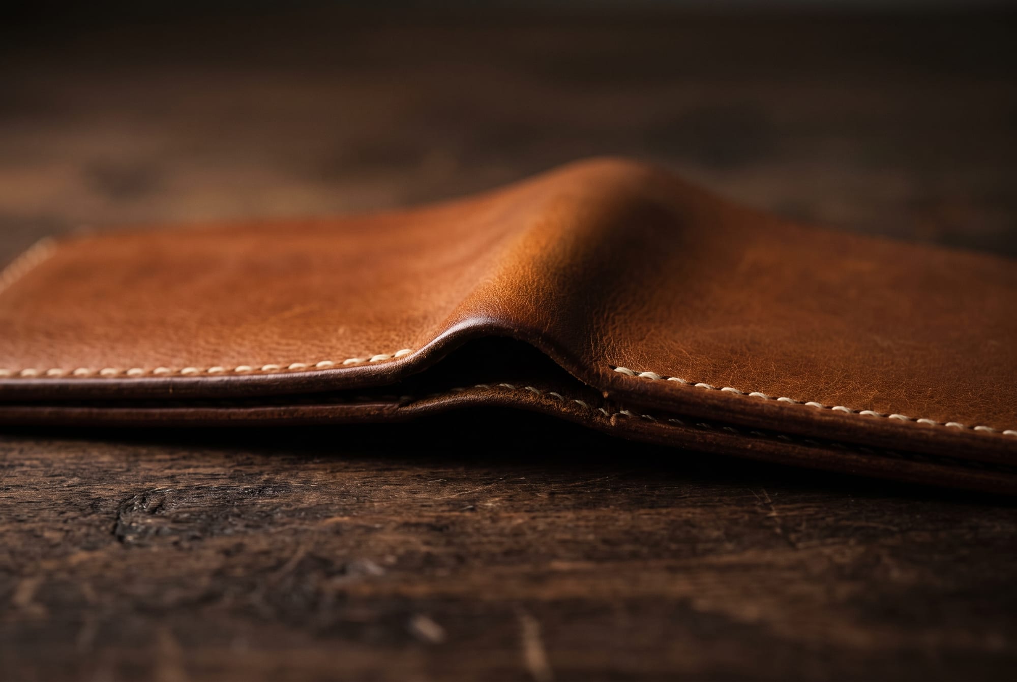 Extreme macro along the mouth of a cognac leather card slot showing the leather skived to a fine taper at the opening, the cut edge burnished smooth, and a line of hand saddle stitching running close to the opening